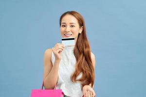 Young asian woman over isolated blue background holding shopping bags and a credit card photo