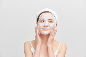 Young girl with facial mask looking at camera over white background. Cosmetic procedure. Beauty spa and cosmetology. photo