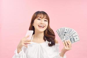 Image of a shocked surprised screaming young pretty woman posing isolated over pink wall background using mobile phone holding money. photo