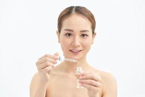 Close-up young Asian woman applying serum on her face. Clean soft make up and isolated white background. photo