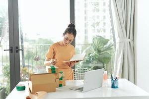 woman checking purchase order in laptop and write in the delivery on package box sell online photo