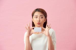 joven mujer hermosa asiática sosteniendo una tarjeta en blanco aislada en un fondo rosa foto