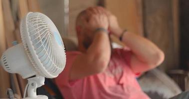 de meester timmerman zit in de buurt de ventilator gedurende de heet tijd van de dag. in echt tijd en langzaam beweging