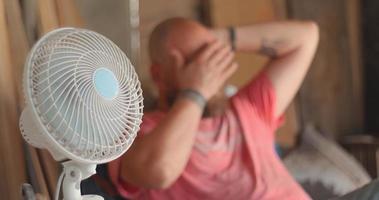 de meester timmerman zit in de buurt de ventilator gedurende de heet tijd van de dag. in echt tijd en langzaam beweging video