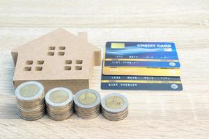 modelo de casa y monedas con tarjeta de crédito en mesa de madera foto