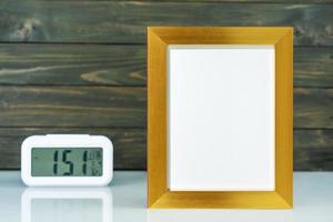 Blank golden frame and digital alarm clock on table photo