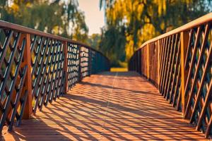 hermoso puente de madera en el bosque de otoño. cálida luz del sol con sombras en el camino hacia el bosque borroso del atardecer. paisaje de otoño estacional naturaleza abstracta al aire libre primer plano. foto