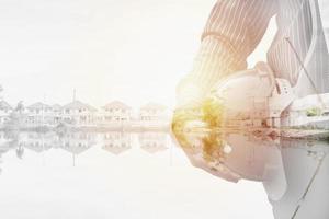 Construction engineer worker hold helmet double exposure with residential new house in progress at building site photo