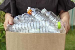 mano que sostiene la caja de basura de reciclaje marrón con botellas de plástico foto