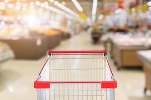 supermarket grocery store with fruit and vegetable shelves interior defocused background with empty red shopping cart photo