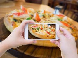 mujer tomando fotos de pizza con teléfono inteligente móvil