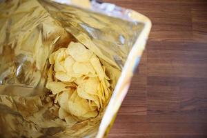 Potato chips in open snack bag close up on table floor photo