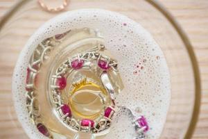 limpiar el anillo de diamantes de joyería vintage y la pulsera en vidrio sobre fondo de mesa de madera foto