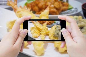 tomando una foto de tempura de camarones en un plato blanco con un teléfono inteligente