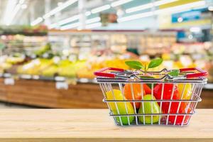 Shopping basket with fruits on wood table over grocery store supermarket blur background photo