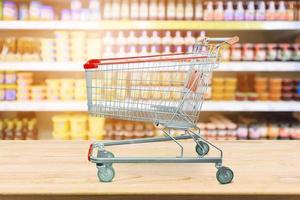 Supermarket with product shelves blur background with empty shopping cart on wood table photo