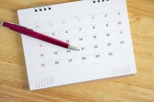 Calendar page with pen on wooden desk table photo