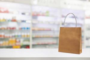 Paper bag on Pharmacy drugstore counter table with medicine and healthcare product on shelves blur background photo