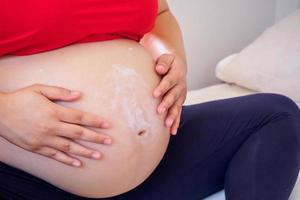 Pregnant Woman applying stretch marks cream on her belly photo