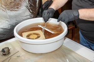 Washing the plastic parts of a very dirty kitchen exhaust fan in an aqueous solution of sodium hydroxide. A man works in protective gloves. photo