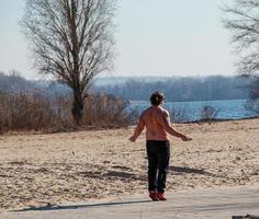 Dnepr, Ukraine - 02.21.2022 A middle-aged man does gymnastics on the river bank. The concept of a healthy lifestyle and the fight against line weight. photo