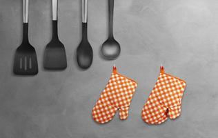 Orange heat resistant cooking gloves with kitchen utensils on cement background