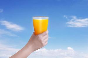 Female hand holding a glass of orange juice against a bright sky background. photo