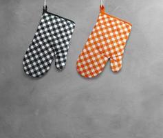 Orange and black heat resistant cooking gloves hanging on a cement wall. photo