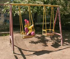 Dnipro, UKRAINE - 05.04.2021 Emotions of a little girl in a yellow jacket and a red cap riding on a swing. photo