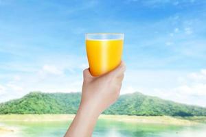 woman holding a glass of orange juice with mountain background beautiful sky Fresh orange juice concept contains vitamin C for health benefits. photo