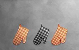 Orange and black heat resistant cooking gloves hanging on a cement wall. photo