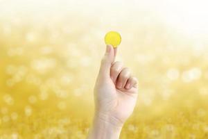 moneda de oro sosteniendo una moneda de oro en la mano sobre un fondo amarillo dorado borroso. foto
