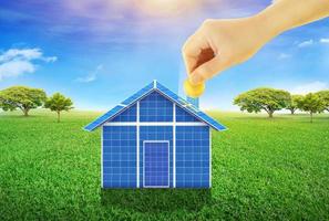 las manos están vertiendo monedas de oro en la casa de células solares. el concepto de energía solar ahorra dinero en las facturas de electricidad. energía pura energía renovable foto
