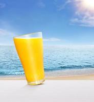 Orange juice in a glass, healthy on white wooden table. with the sky and the sea in the background photo