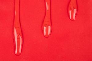transparent varnish, clear oil drops on red paper copy space background photo
