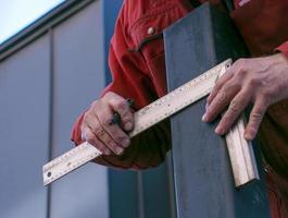 A skilled worker measures and marks a line on a square pipe with an iron ruler for further cutting photo