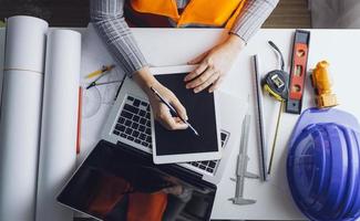 Two colleagues discussing data working and tablet, laptop with on on architectural project at construction site at desk in office photo