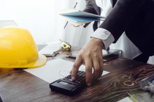 Two colleagues discussing data working and tablet, laptop with on on architectural project at construction site at desk in office photo