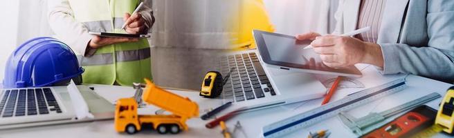 Two colleagues discussing data working and tablet, laptop with on on architectural project at construction site at desk in office photo