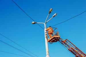 un trabajador municipal en equipo de protección realiza un trabajo peligroso para eliminar una interrupción en la red eléctrica. un trabajador repara una farola desde una cesta de plataforma aérea. foto