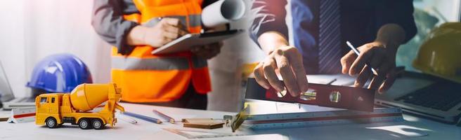 Two colleagues discussing data working and tablet, laptop with on on architectural project at construction site at desk in office photo