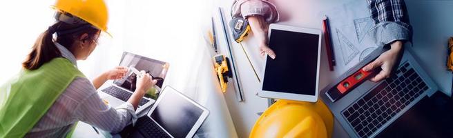 Two colleagues discussing data working and tablet, laptop with on on architectural project at construction site at desk in office photo