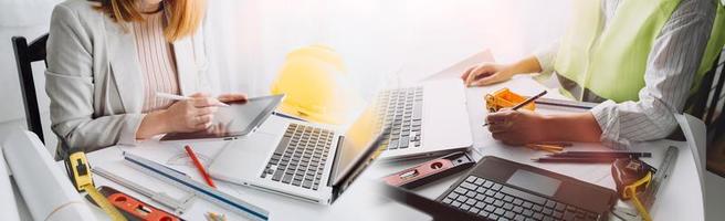 Two colleagues discussing data working and tablet, laptop with on on architectural project at construction site at desk in office photo