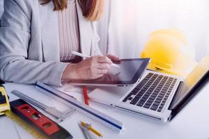 Two colleagues discussing data working and tablet, laptop with on on architectural project at construction site at desk in office photo