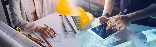 Two colleagues discussing data working and tablet, laptop with on on architectural project at construction site at desk in office photo