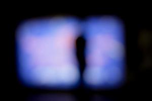 Lens blur image of a blurry male silhouette standing on front of a large screen. photo