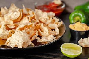 Close up Hand hold chip dip tomato salsa with plate with taco, nachos chips and tomato dip. Spicy Nachos  on rustic wooden background photo