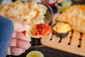 Close up Hand hold chip dip tomato salsa with plate with taco, nachos chips and tomato dip. Spicy Nachos  on rustic wooden background photo