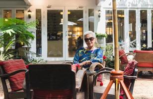 Portrait of senior woman in sunglasses sitting on a chair in cafe outdoor. photo