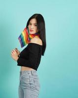 LGBTQ woman holding pride flag standing against a blue green background. photo